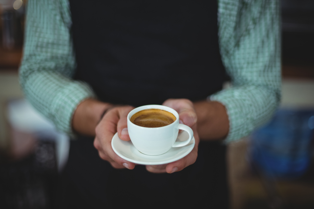 Mid section of waiter holding cup of coffee in cafe